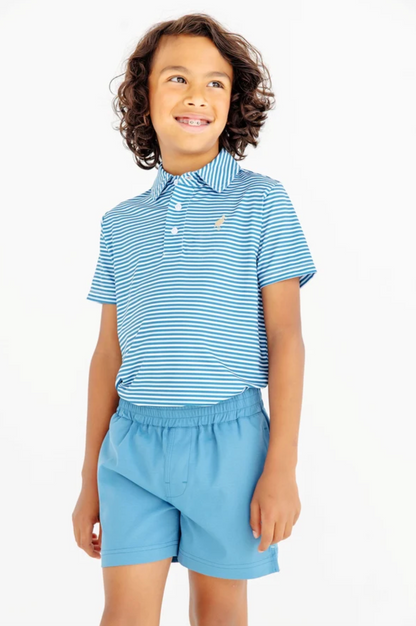 A young boy with curly brown hair wearing a light blue and white striped polo shirt with a small embroidered logo on the chest, paired with light blue shorts, against a plain white background.